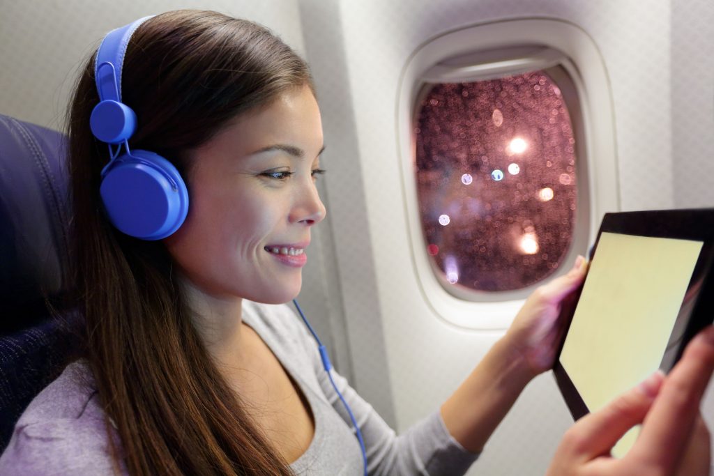 32105389 - passenger in airplane using tablet computer. woman in plane cabin using smart device listening to music on headphones.